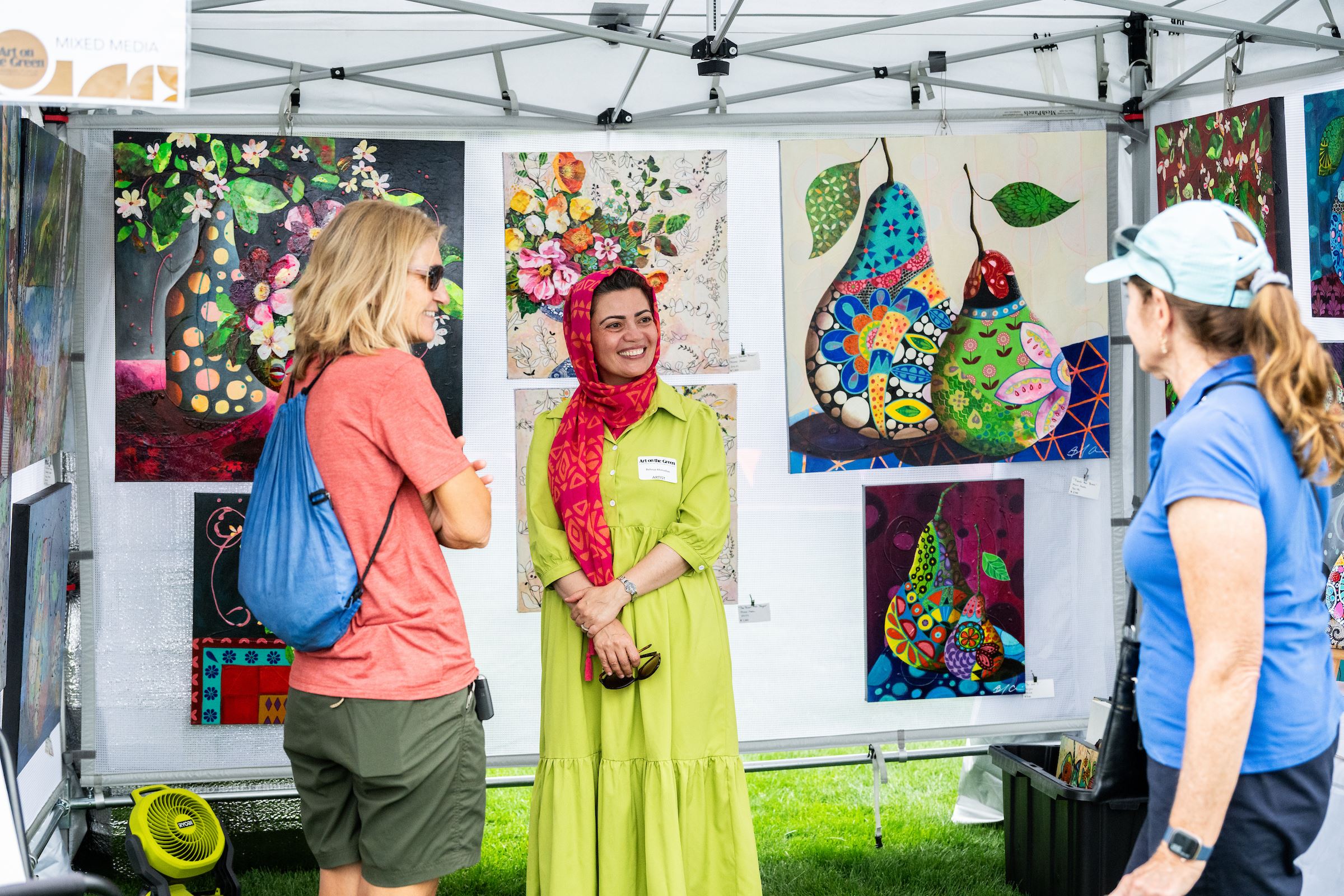 Artist smiles at visitors to her booth that displays colorful paintings