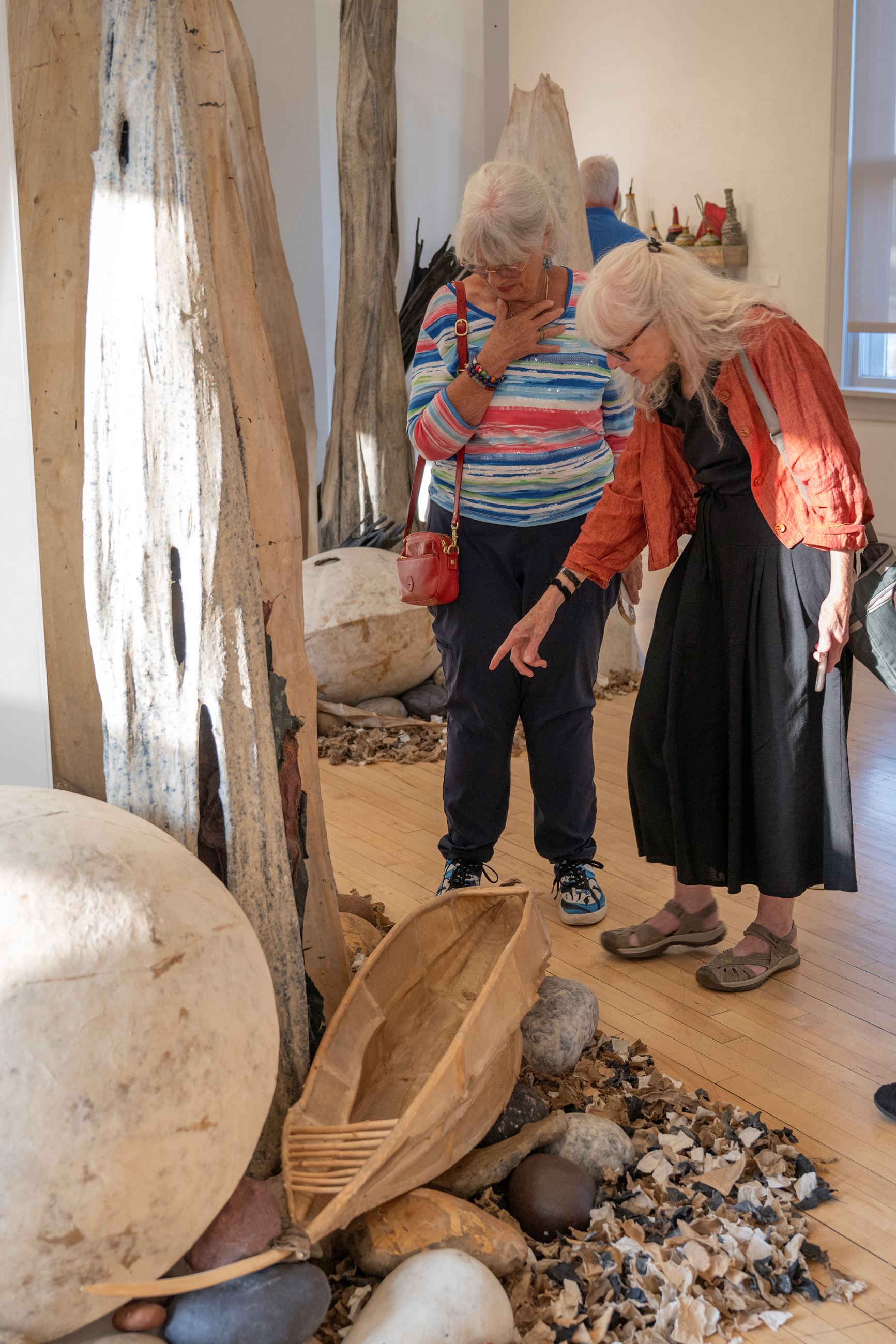 Two visitors pointing and looking down at fiber and paper artworks.